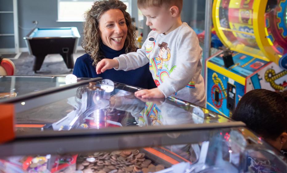 Young boy playing arcade machines with Mum watching on at Woolacombe Sands Holiday Park